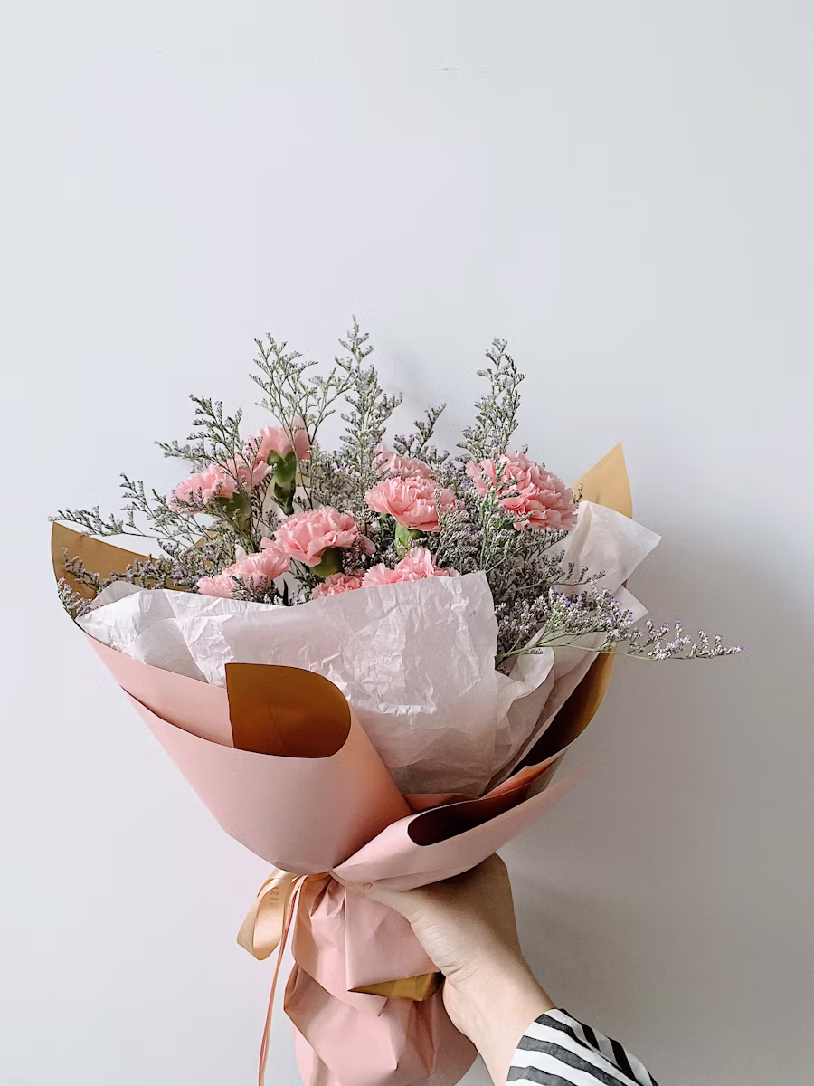 Bouquet d'œillets roses et statices argentés, papier rose pâle, tenu en main