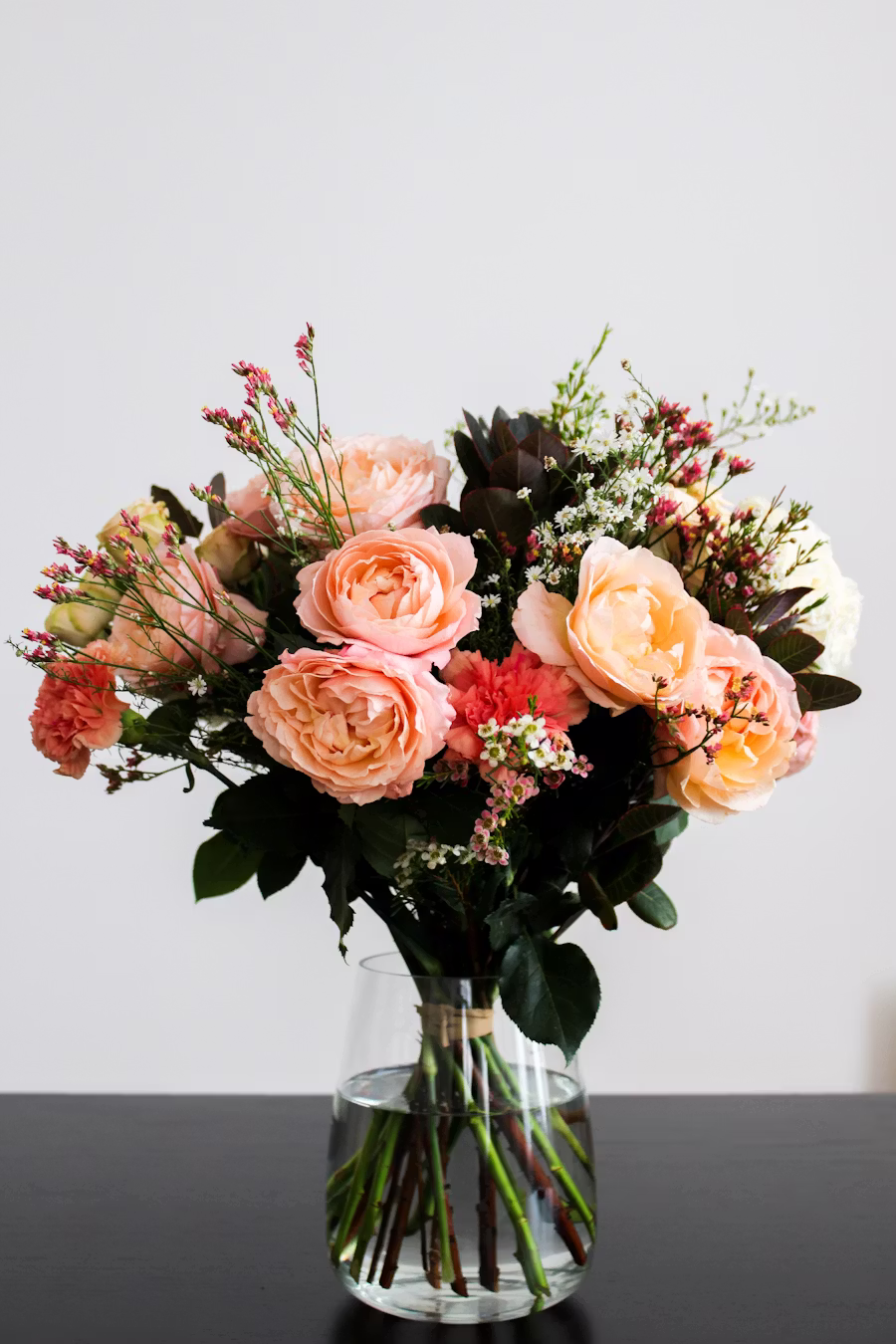 Bouquet de roses anciennes orange et saumon disposé dans un vase en verre, sur fond clair