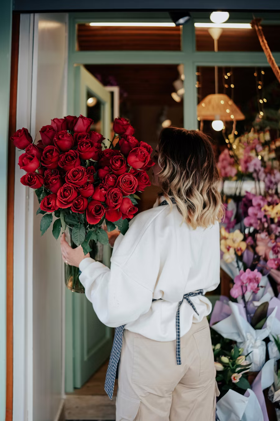 Femme tenant un grand bouquet de roses rouges devant la devanture verte de la boutique Maison Garance, intérieur visible avec d'autres bouquets